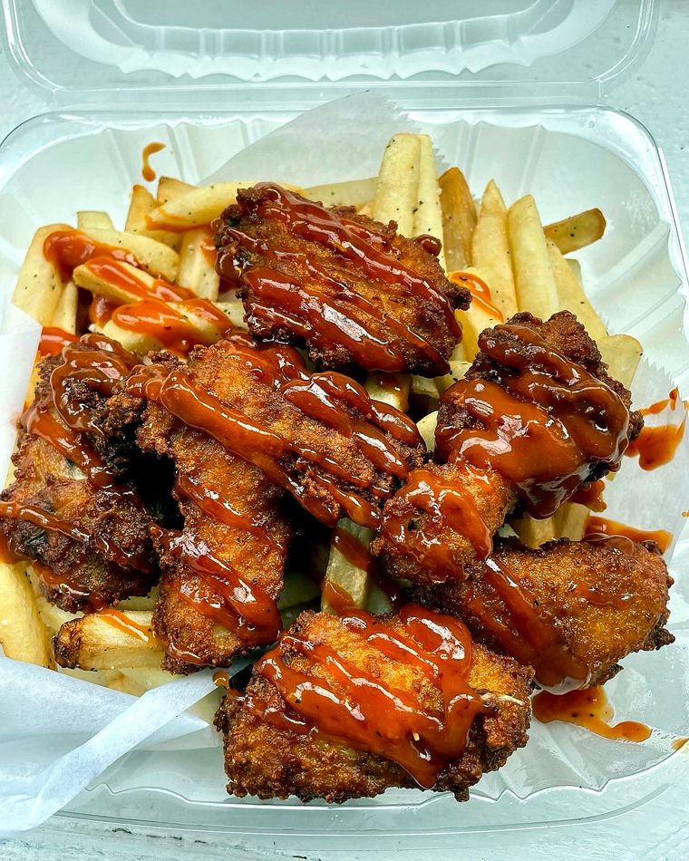 Party wings drizzled with sauce over french fries in a takeout box at Corner Café